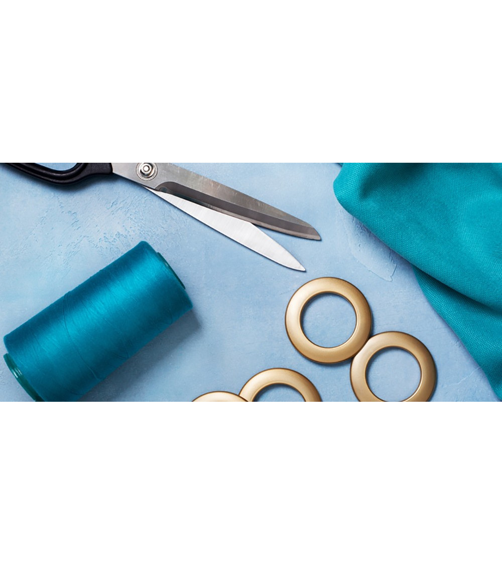 Œillets clipsables dorés posés sur un tissu bleu, à côté d'une paire de ciseaux
